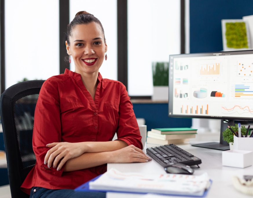 Portrait of business woman in corporate office sitting at desk smiling at camera. Company executive leadership working on financial statistics. worker doing charts on computer.